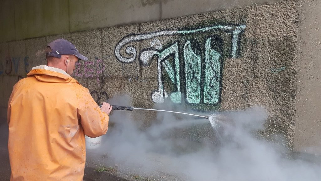 Medewerker verwijdert graffiti van betonnen muur met hogedruk stoomreiniger