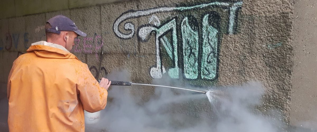 Medewerker verwijdert graffiti van betonnen muur met hogedruk stoomreiniger