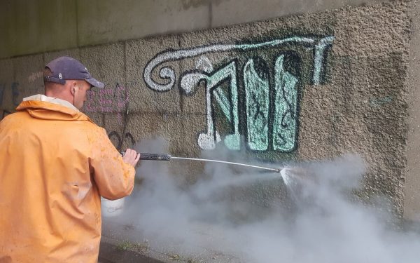 Medewerker verwijdert graffiti van betonnen muur met hogedruk stoomreiniger