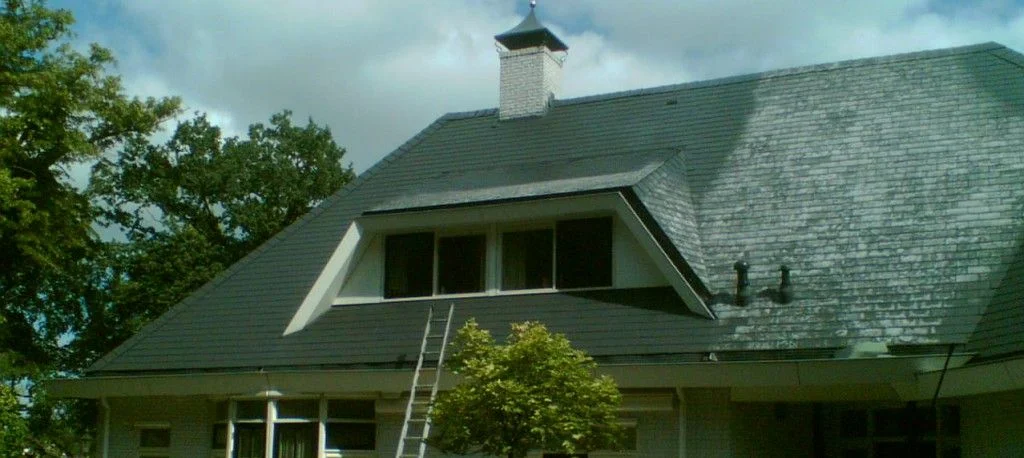 Dakrenovatie met vervanging van grijze dakpannen op woonhuis met ladder tegen gevel geplaatst