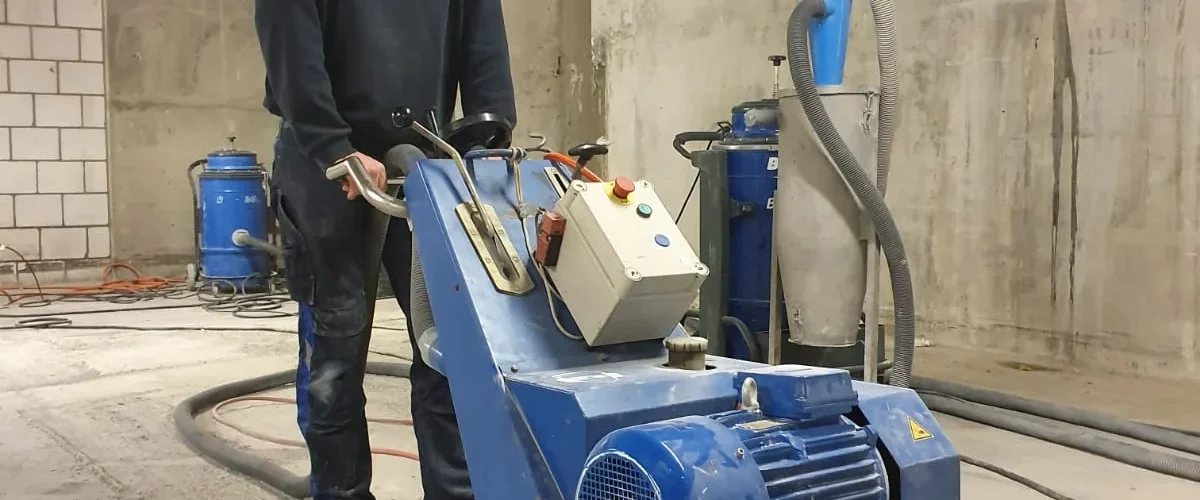 Medewerker freest betonvloer in parkeergarage met professionele vloesfreesmachine voor gelijkmaken ondergrond