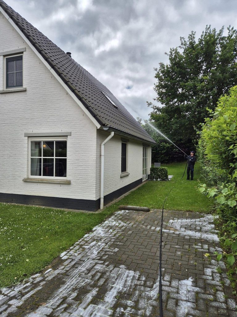 Professionele gevelreiniging van witte woning met donker pannendak en tegelpaden in Overijssel