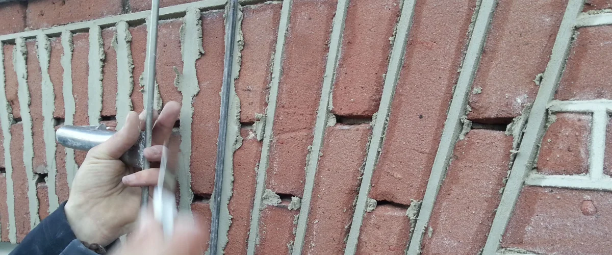 Hand bevestigt of verwijdert metalen hekwerk voor rode bakstenen muur tijdens sloop- of renovatiewerkzaamheden