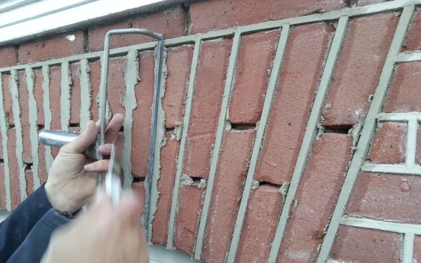 Hand bevestigt of verwijdert metalen hekwerk voor rode bakstenen muur tijdens sloop- of renovatiewerkzaamheden