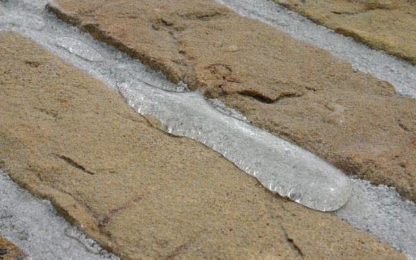 Voegzand wordt aangebracht tussen betonnen bestratingstegels voor afwerking van verharding