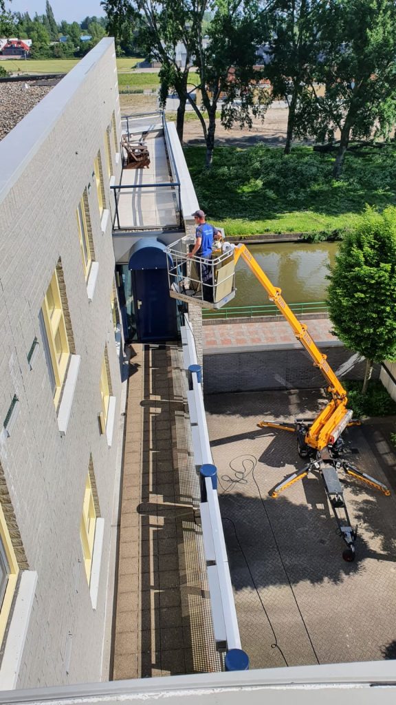 Professionele gevelreiniging met hoogwerker aan betonnen bedrijfspand