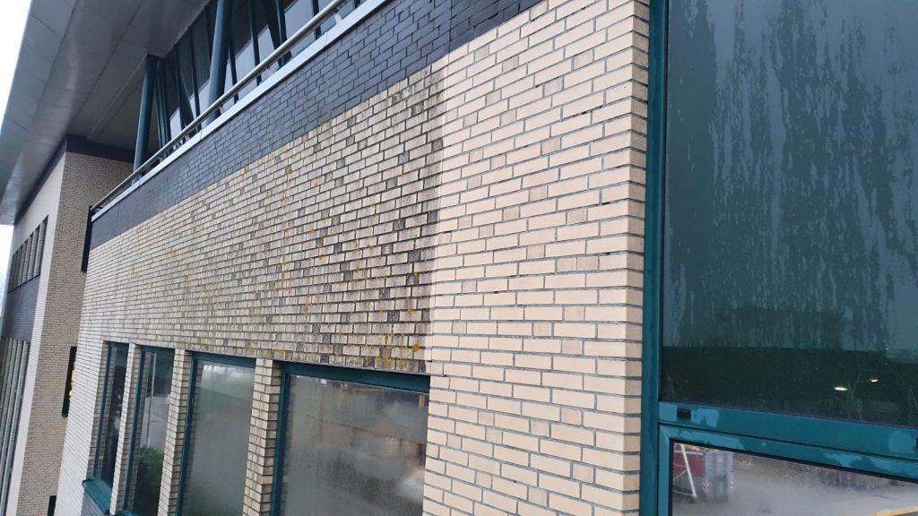 Professionele reiniging van lichte bakstenen gevel met donkere groene panelen en raampartijen