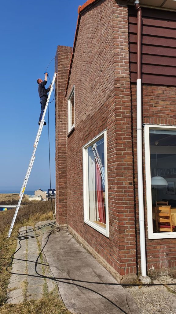 Professionele gevelreiniging van bakstenen muur met hoogwerker bij woning