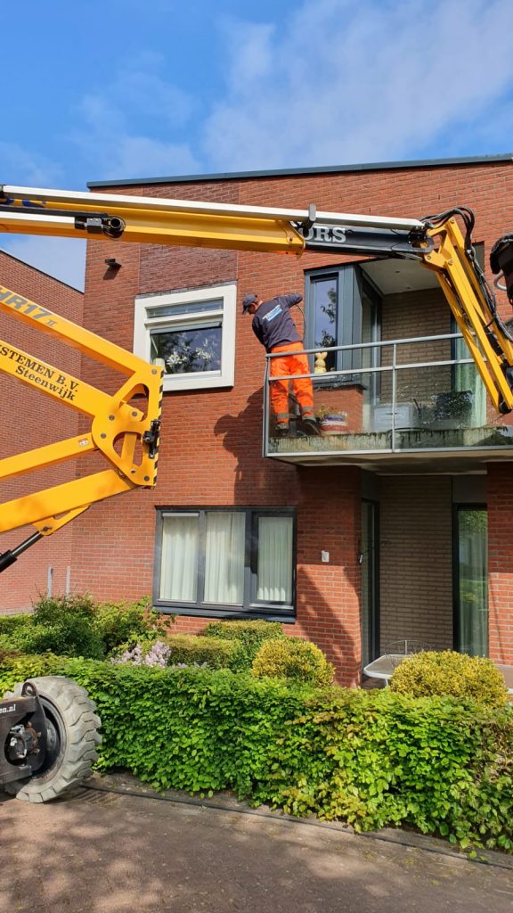 Professionele gevelreiniging met gele hoogwerker bij moderne bedrijfspand met rode gevelbekleding