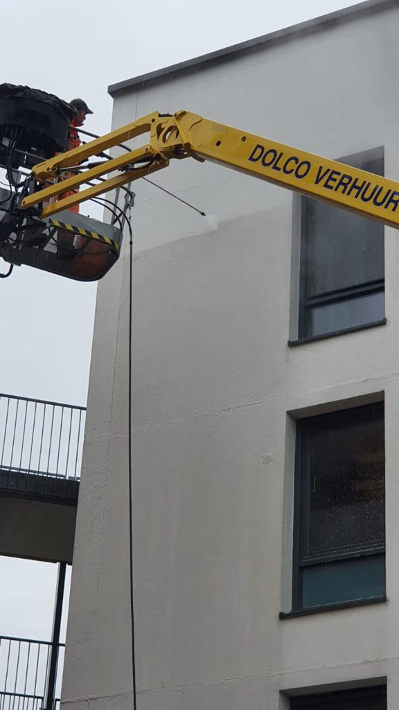 Gevelreiniging met gele hoogwerker aan appartementengebouw, professionele reiniging op hoogte
